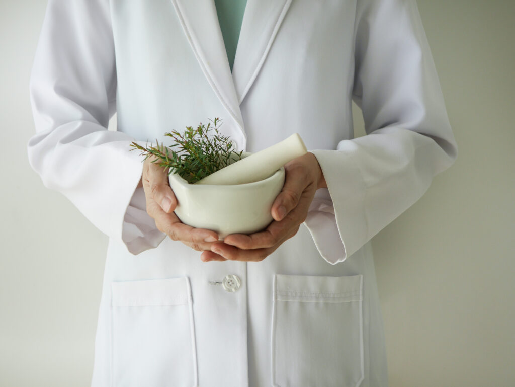 Hände halten einen weißen Mörser mit frischen Kräutern – Naturheilkunde bei Autoimmunerkrankungen als Ergänzung zur Medizin